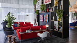 A modern living room with a red sofa, a black bookshelf, and a large window with sheer curtains.