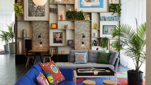 Una sala de estar moderna con un sofá azul, cojines coloridos, una mesa de centro y una estantería llena de libros y objetos decorativos.
