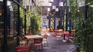 Un comedor interior con mesas y sillas, ventanas amplias y lámparas colgantes.