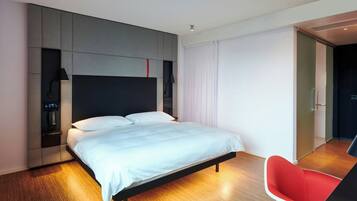 A modern hotel room with a large bed, a red chair, and a built-in desk.