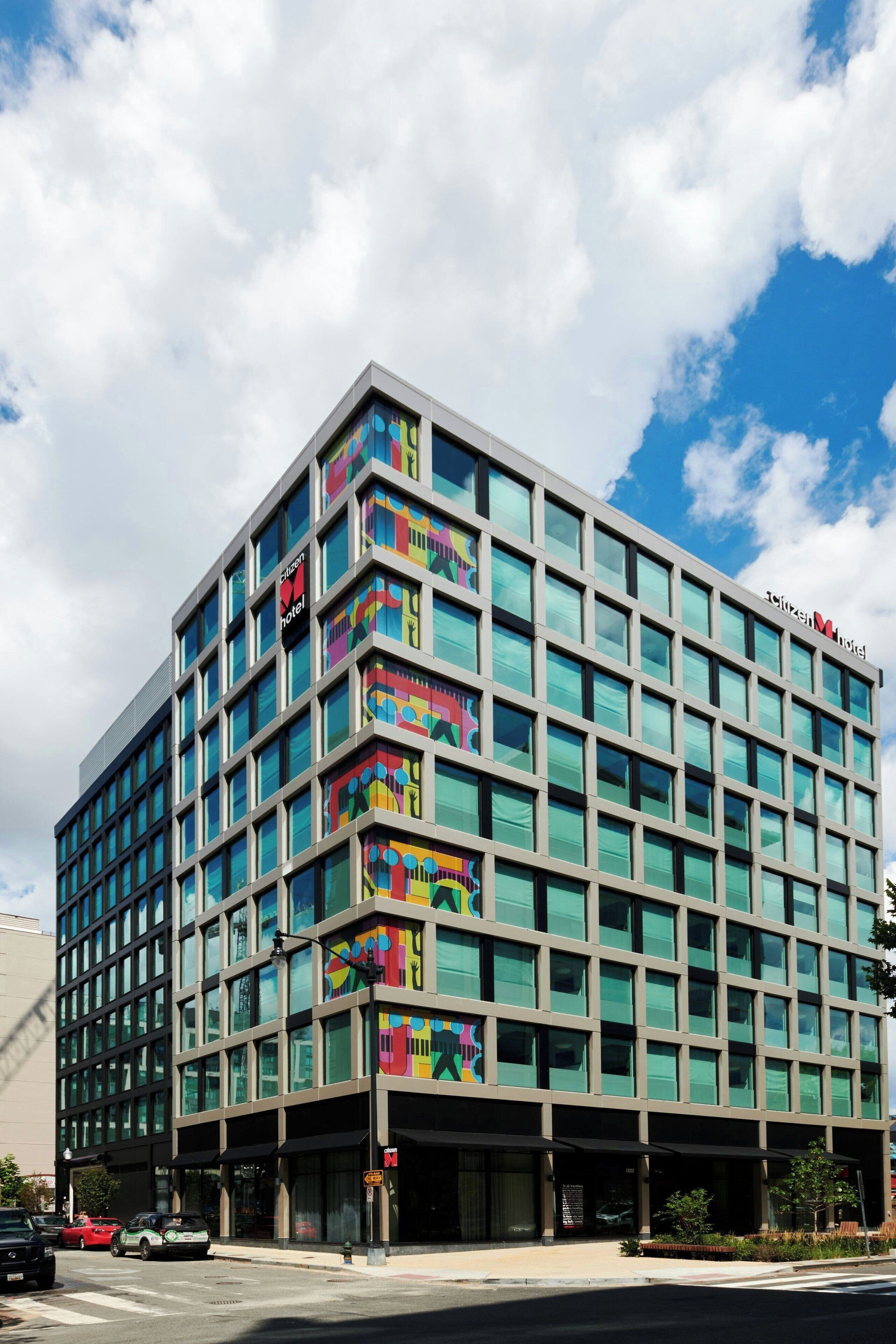 A modern hotel with a glass facade, multiple floors, and a colorful mural on the side.