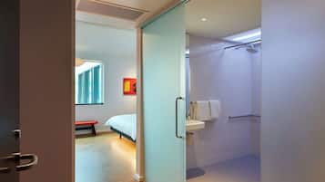 Una habitación de hotel moderna con una cama, un banco, una ducha y un lavabo.