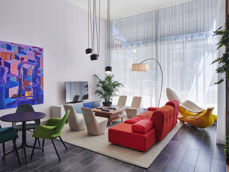 A modern living room with a red sofa, green and beige chairs, a round table, and a large abstract painting on the wall.