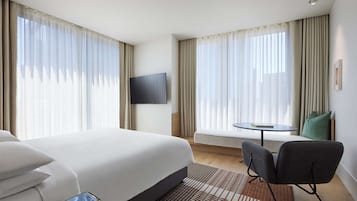 A hotel room with a large bed, a flat-screen TV, a small table with a chair, and a sofa with a pillow.