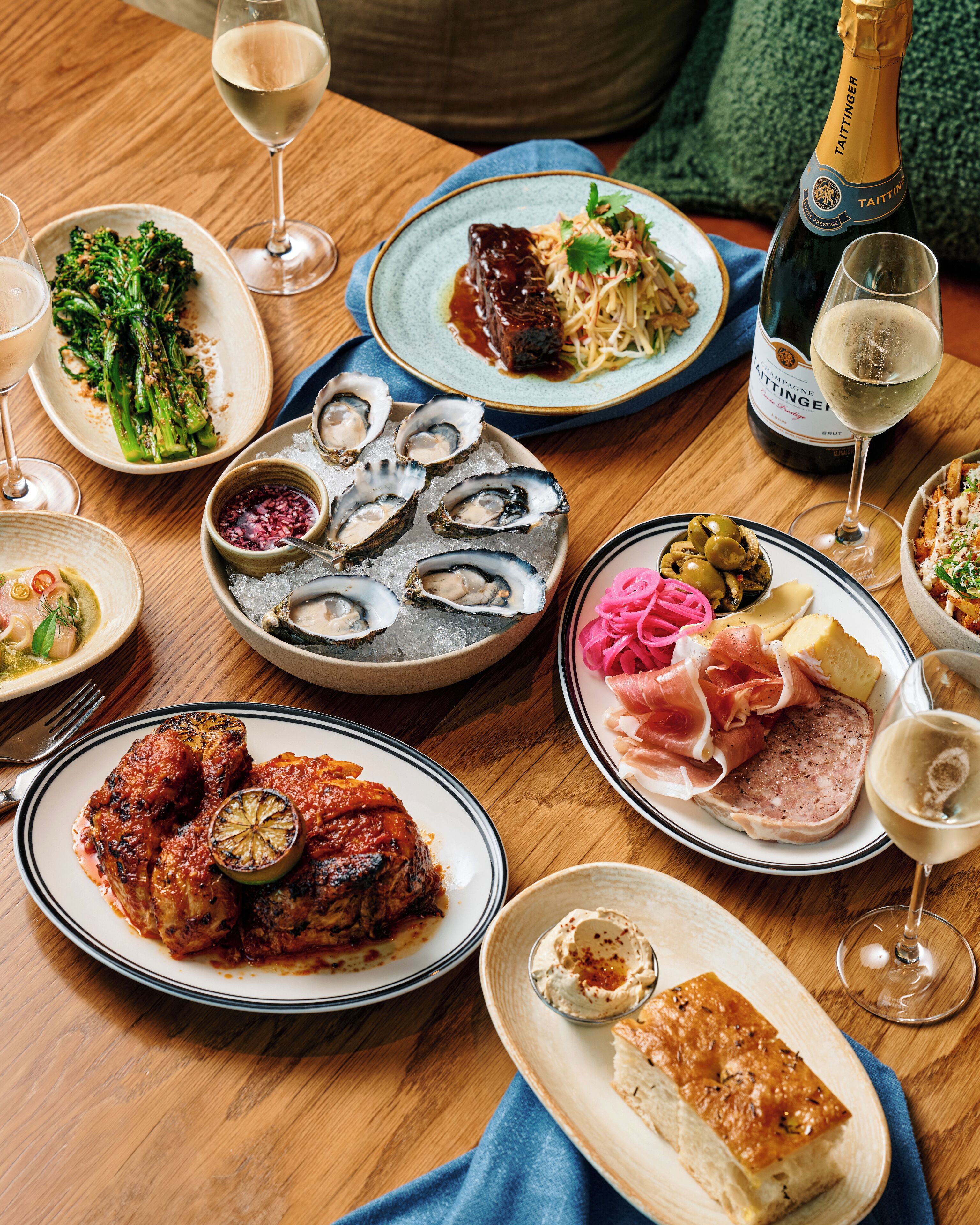Diversos pratos sobre uma mesa de madeira, incluindo frutos do mar, carnes e legumes, com copos de vinho.