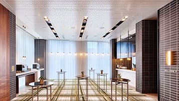 A modern hotel lobby with a check-in counter, seating area, and a kitchen visible in the background.