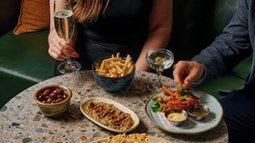 Una mesa con varios platos, incluyendo un cuenco de aceitunas, una porción de papas fritas y un plato con salsa verde.
