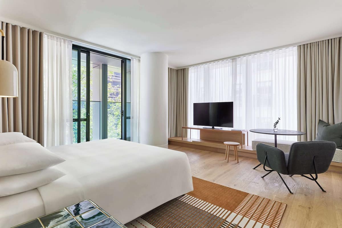 A hotel room with a large bed, a TV, a small table, and a chair.