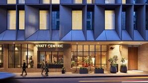 A modern hotel facade with large windows, a visible entrance, and outdoor seating with potted plants. - Hyatt Centric Melbourne (Melbourne)