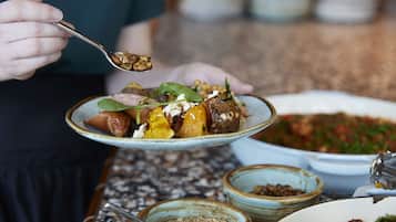 A person holding a plate with food, a bowl of salad, and a pepper grinder on a table.