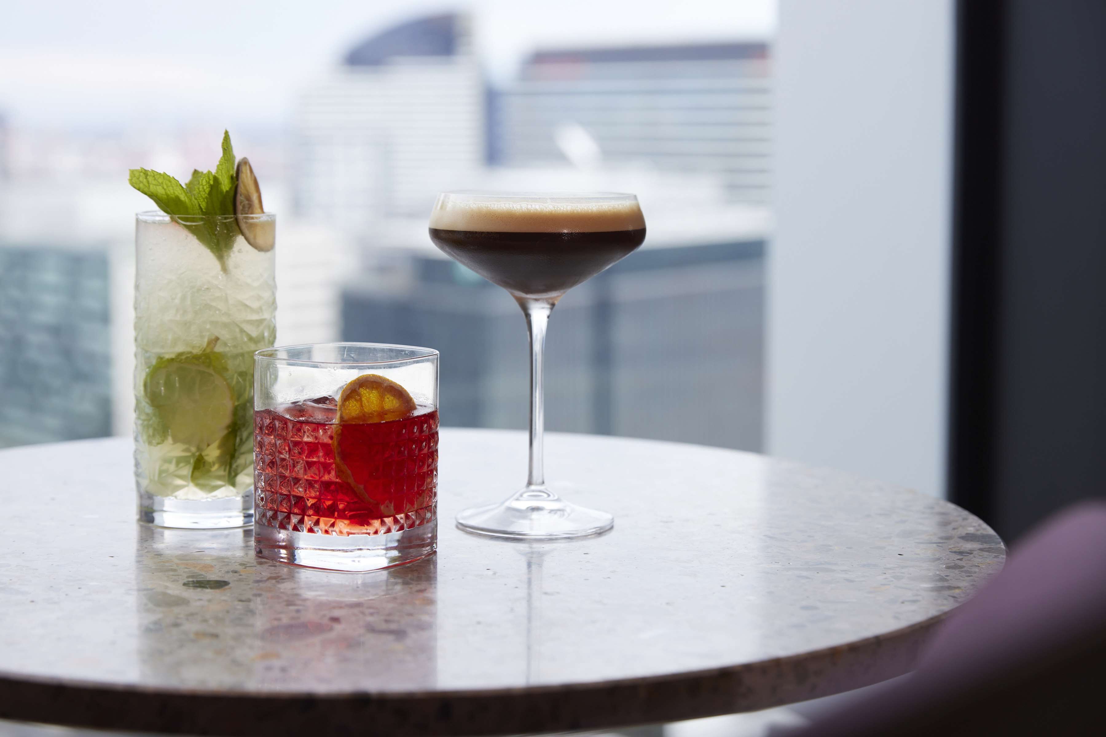 Tres bebidas sobre una mesa con una vista urbana de fondo.