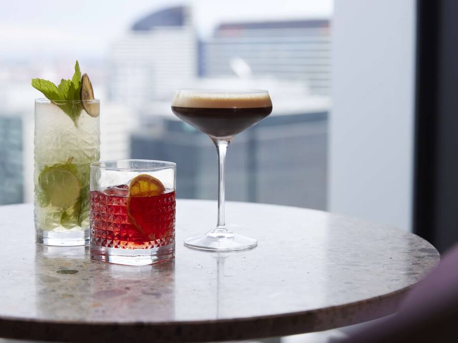 Tres bebidas sobre una mesa con una vista urbana de fondo.
