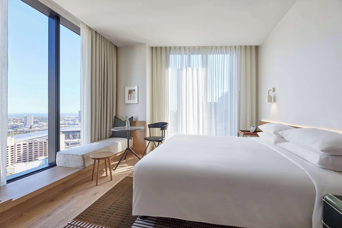 A modern hotel room with a large bed, a small desk, a chair, and a view of the city.