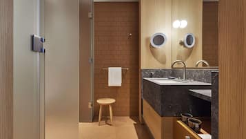 A modern bathroom with a wooden vanity, two round mirrors, a sink, and a small stool.
