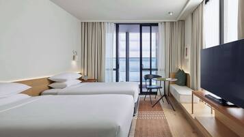 Habitación de hotel con dos camas, un televisor, una mesita y vista a la ciudad.