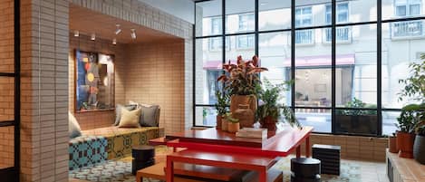 Un interior moderno con pared de ladrillo, un ventanal grande, una mesa roja y diversas plantas.