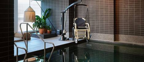 A modern indoor pool with a wheelchair-accessible area, a potted plant, and a hanging light fixture.
