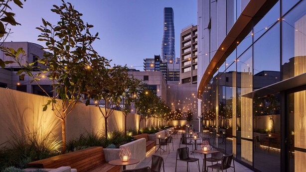 An outdoor patio with seating, string lights, and a view of modern buildings. - Hyatt Centric Melbourne (Melbourne)