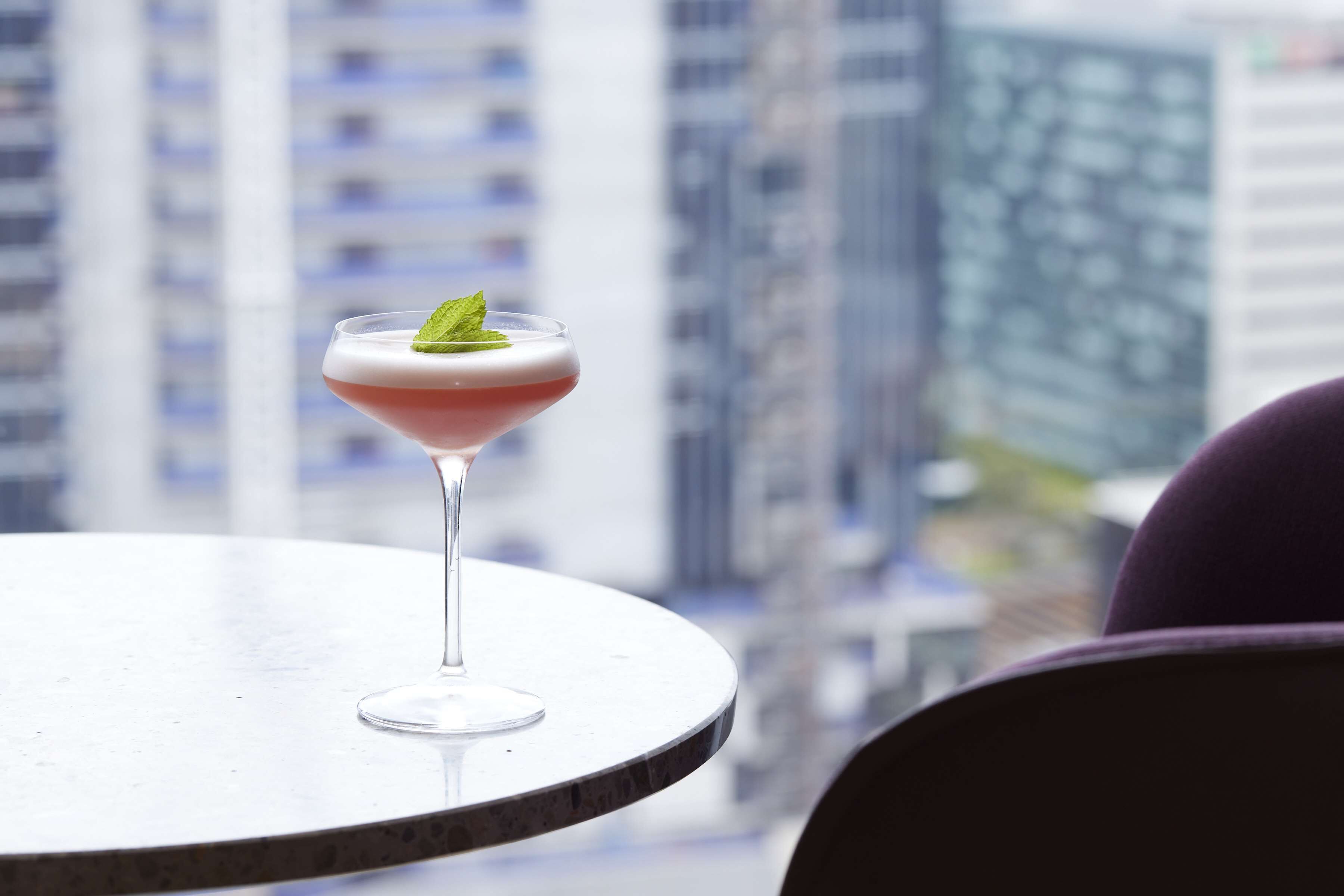 A martini glass with a mint garnish on a round table with a cityscape view in the background.