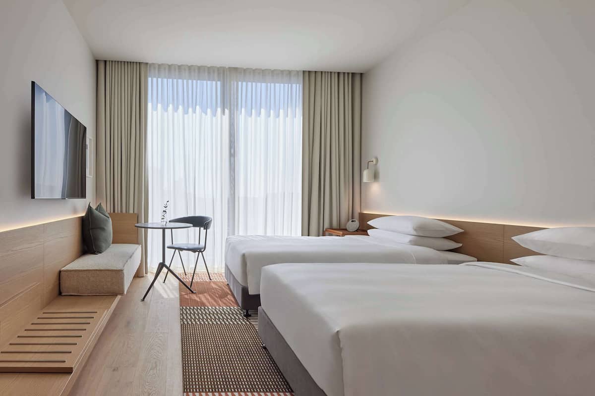 A hotel room with two beds, a sofa, a TV, a small table, and a chair.