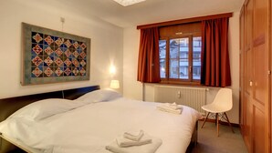 Quarto de hotel com cama grande, obra de arte acolchoada na parede, janela com cortinas e radiador.