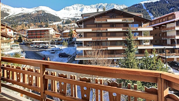 Um resort de montanha com edifícios de vários andares, área de estacionamento e montanhas cobertas de neve ao fundo.