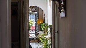 A narrow hallway with a tiled floor, leading to a room with a large window and a decorative iron gate. - Portus Gaditanus s XVIII Patio Andaluz (El Puerto de Santa Maria)
