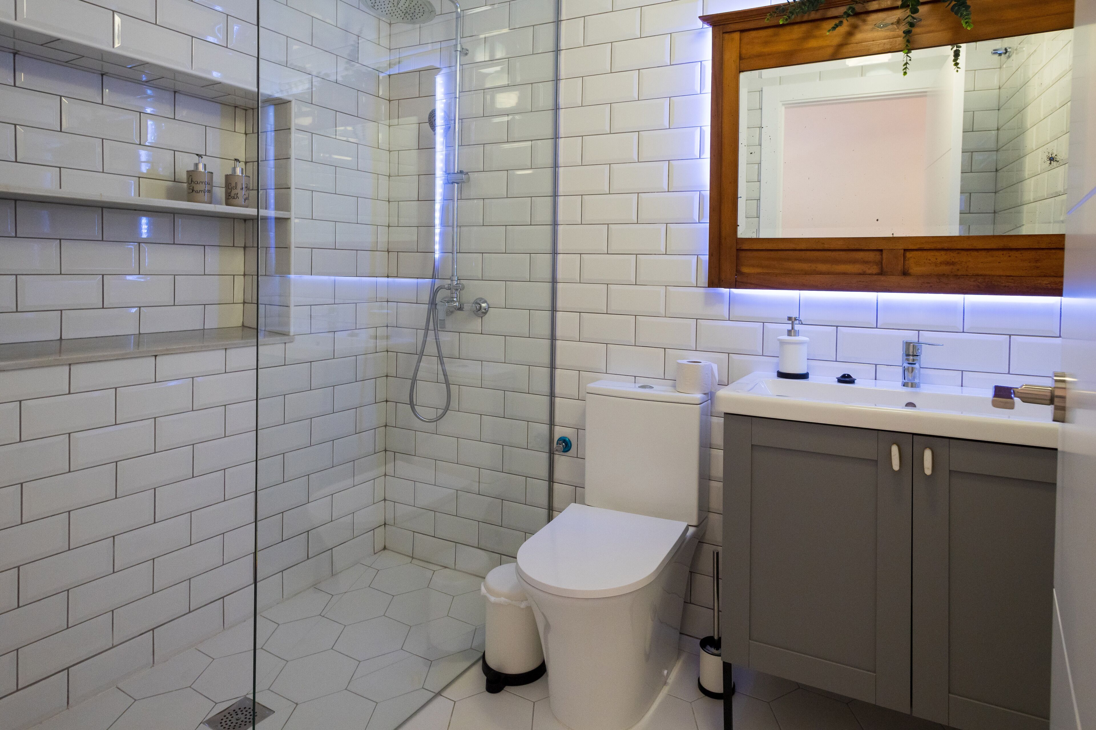 Un baño moderno con azulejos blancos tipo metro, ducha con cerramiento de vidrio, inodoro y tocador con espejo.