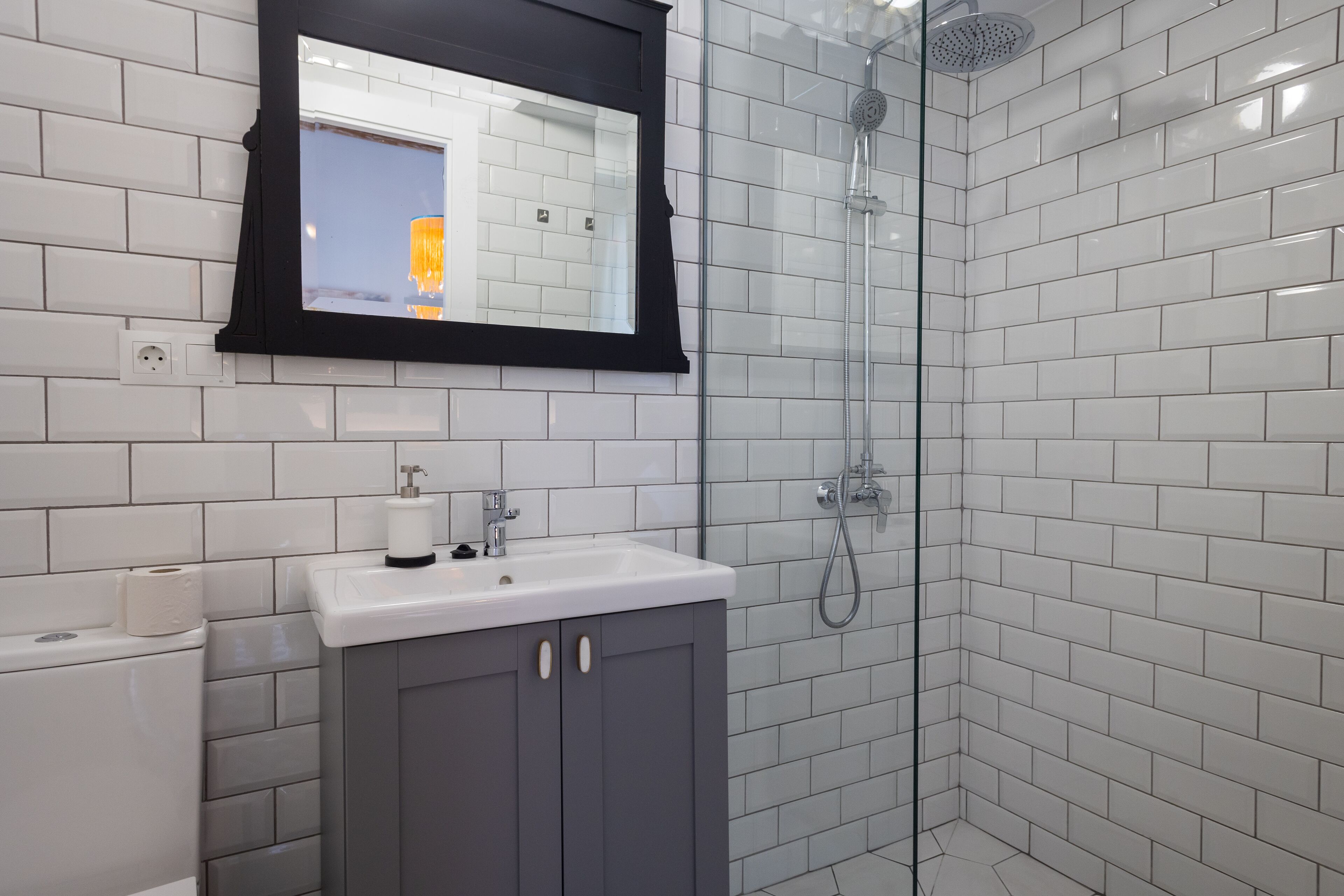 A modern bathroom with white tiles, a glass shower enclosure, and a sink with a mirror above it.