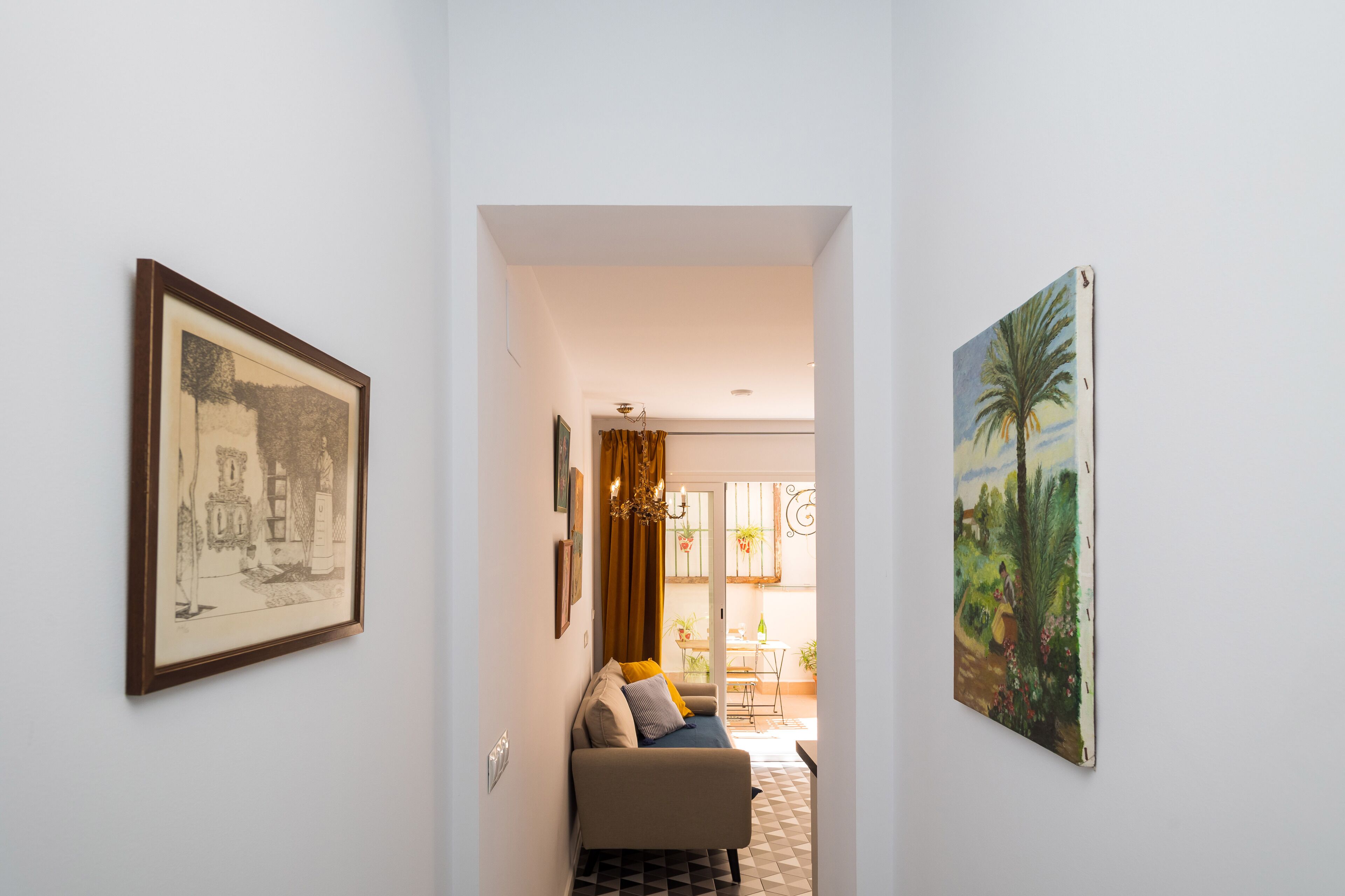 A hallway with a sofa, framed artwork, and a view into a dining area.