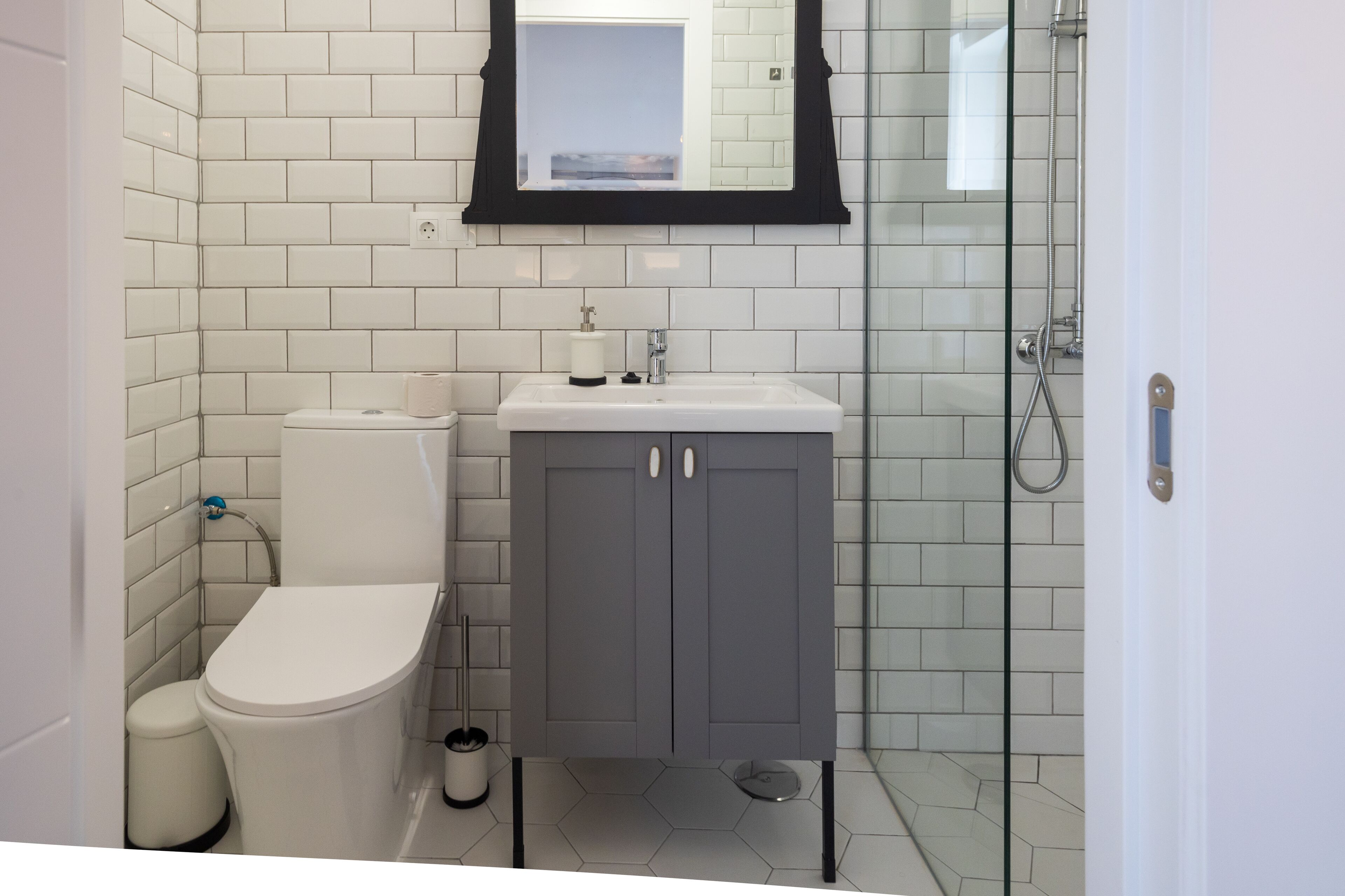 Un bagno moderno con piastrelle bianche stile metro, un water bianco, un mobile contenitore grigio e un box doccia in vetro.
