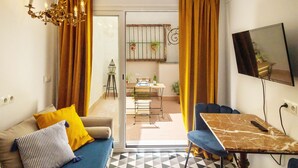 A living room with a sofa, a table, a TV, and a view into the dining area. - Portus Gaditanus s XVIII Patio Andaluz (El Puerto de Santa Maria)