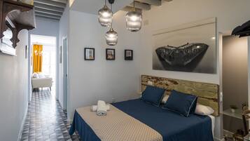 A bedroom with a bed, a headboard, a wall-mounted artwork, and a hallway leading to a bathroom.