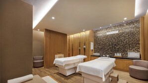 Un moderno cuarto de spa con dos camillas de masaje, un mostrador de recepción y una pared con diseño de mosaicos.