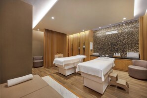 A modern spa room with two massage tables, a reception desk, and a wall with a mosaic pattern.