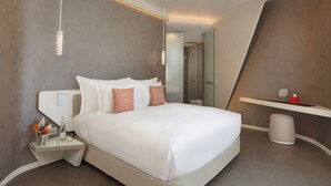 Una habitación de hotel moderna con una cama grande, mesitas de noche, un espejo y zona de ducha.