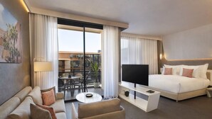 A modern hotel room with a bed, a TV, a sofa, a coffee table, and a balcony with a view of buildings. - Pestana Cr7 Marrakech (Marrakech)