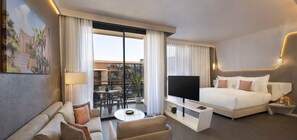 A modern hotel room with a bed, a TV, a sofa, a coffee table, and a balcony with a view of buildings.
