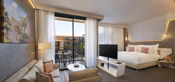 A modern hotel room with a bed, a TV, a sofa, a coffee table, and a balcony with a view of buildings.