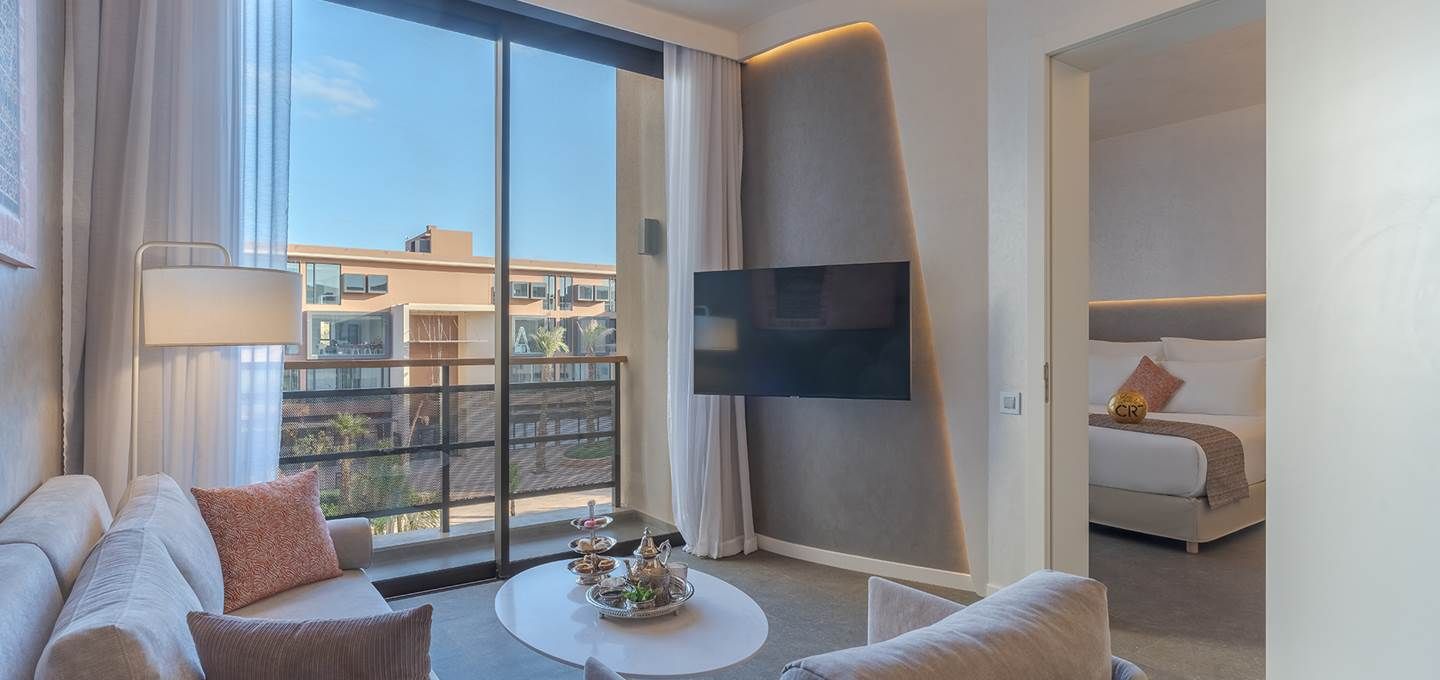 Quarto de hotel moderno com uma janela grande, televisão de tela plana, sofá, mesa de centro e cama.