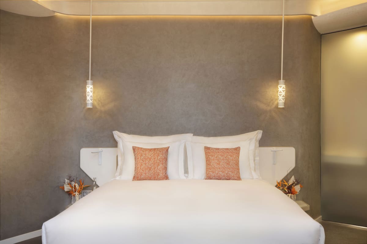 Een moderne hotelkamer met een groot bed, twee wandlampen en een nachtkastje met een bloemenvaas.