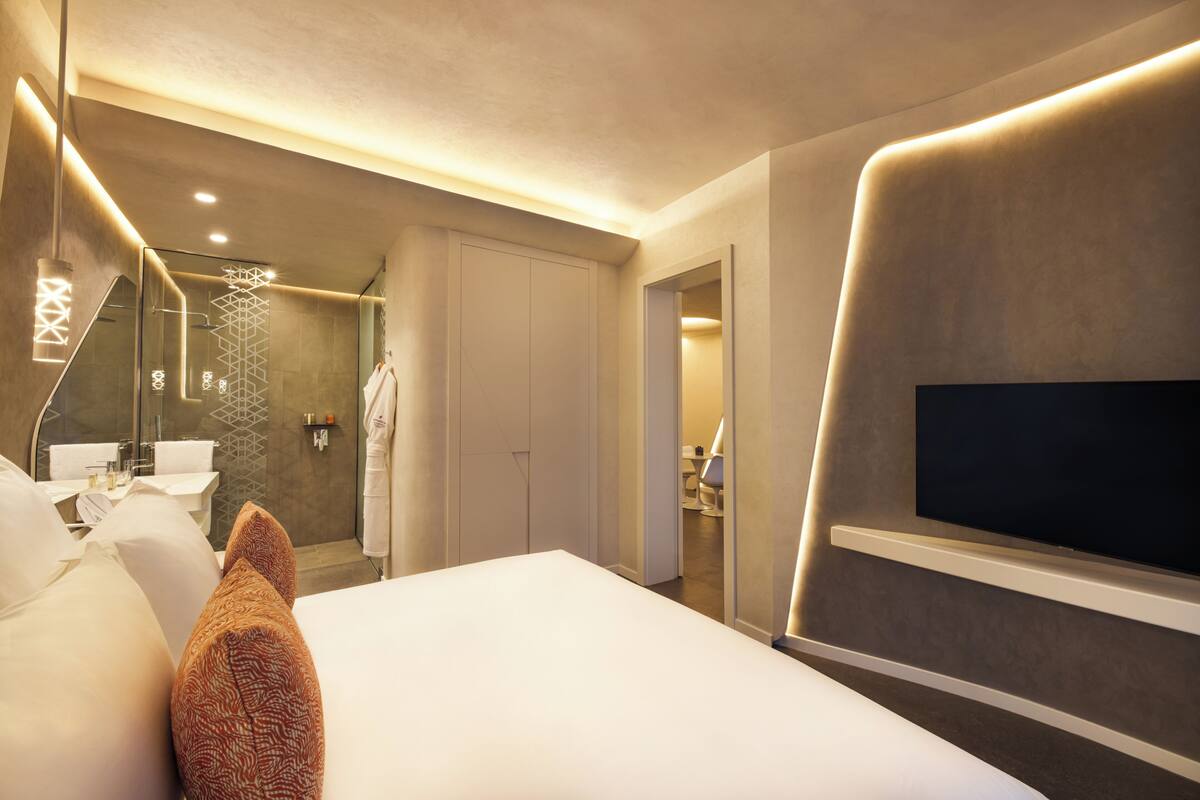 Een moderne hotelkamer met een groot bed, een aan de muur bevestigde televisie, een badkamer met een glazen douche en een inloopkast.