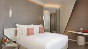 Una habitación de hotel moderna con una cama grande, mesitas de noche, un espejo y zona de ducha.