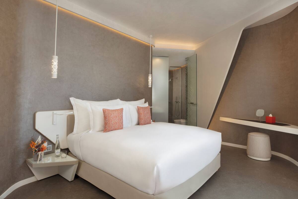 Een moderne hotelkamer met een groot bed, nachtkastjes, een spiegel en een douche.