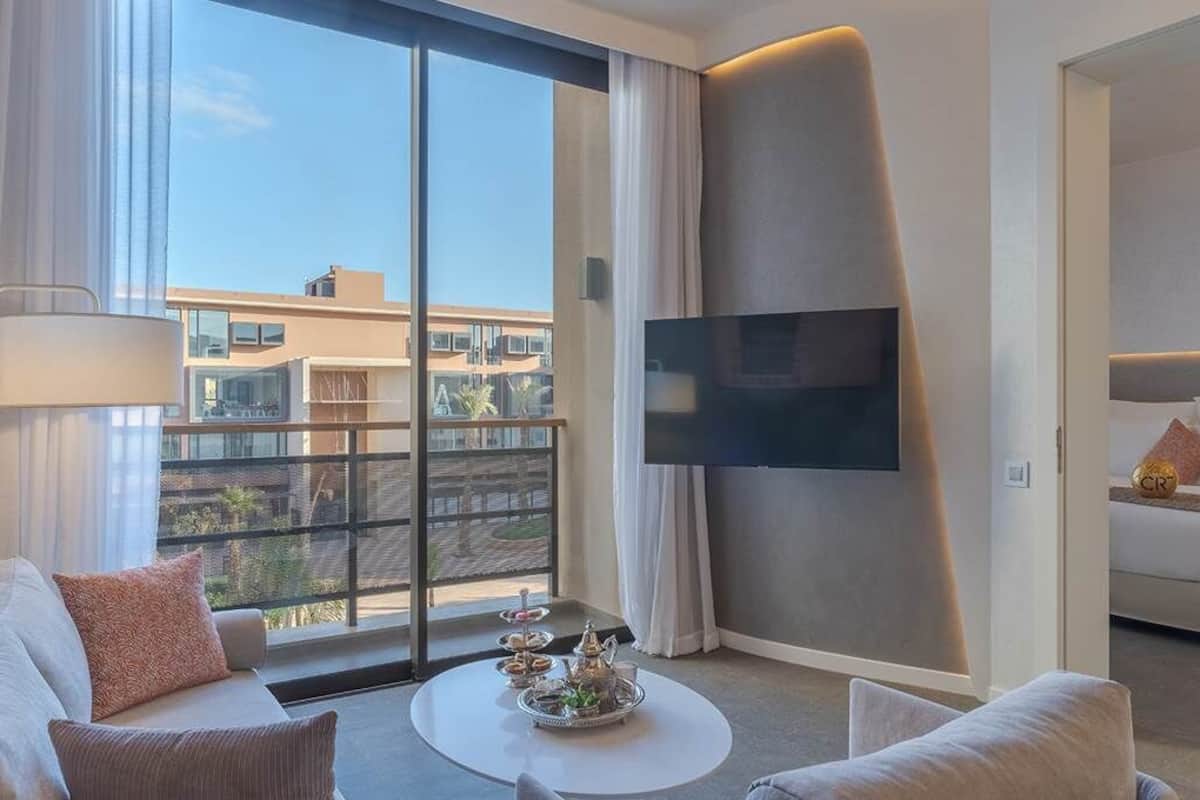 Een moderne hotelkamer met een groot raam, een flatscreen televisie, een bank, een bijzettafeltje en een bed.