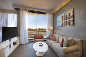 A modern hotel room with a flat-screen TV, a sofa, a coffee table, and a large window offering a city view. - Pestana Cr7 Marrakech (Marrakech)