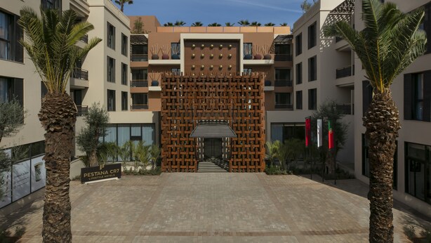 A modern hotel entrance with a geometric facade, palm trees, and a clear sky. - Pestana Cr7 Marrakech (Marrakech)
