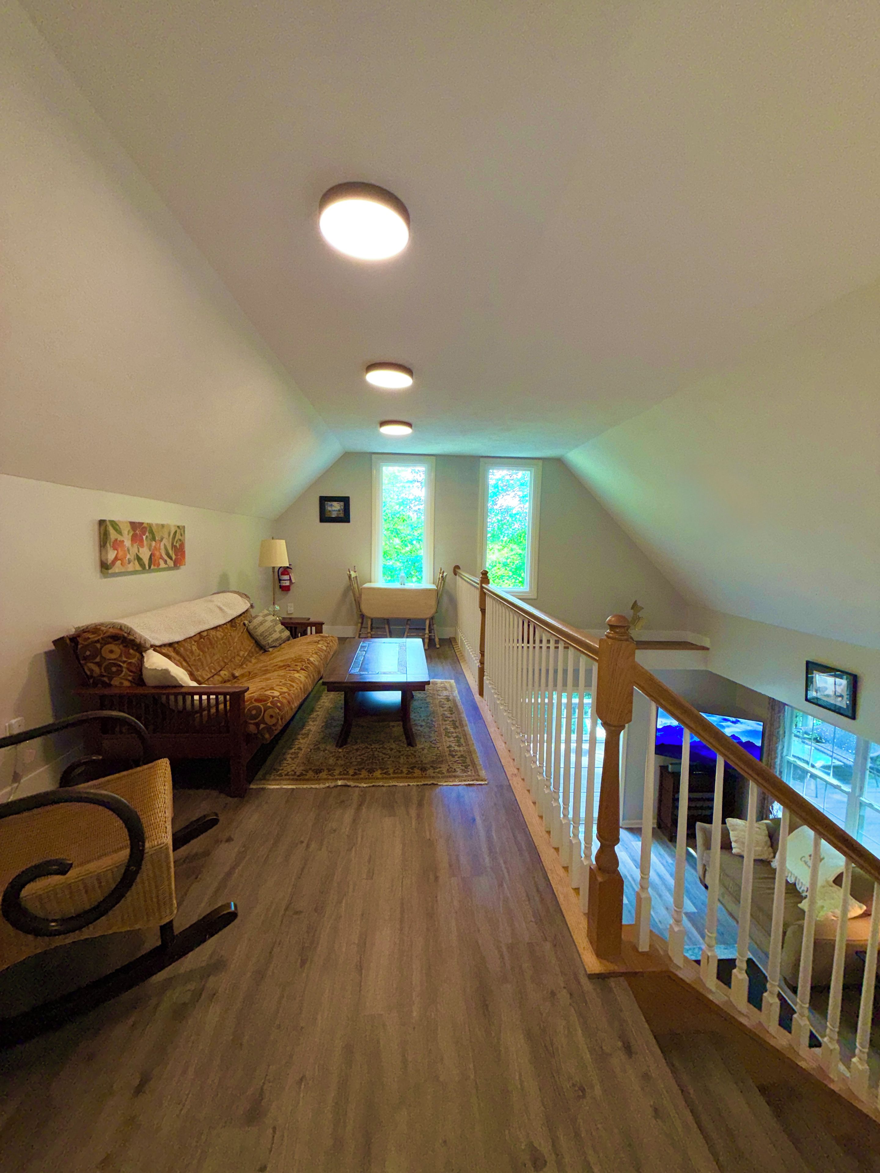 A spacious living room with a wooden floor, a sofa, a dining table, and a staircase leading to an upper level.