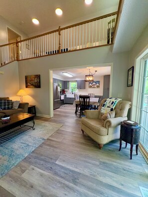 A spacious living room with a high ceiling, a staircase, and a view into the kitchen area.