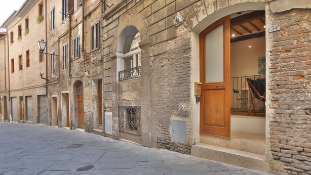 A narrow street lined with historic stone buildings, featuring arched doorways and wooden shutters. - Independent apartment near Piazza del Campo (Siena)